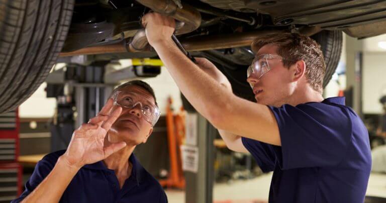 collision repairers at work under vehicle